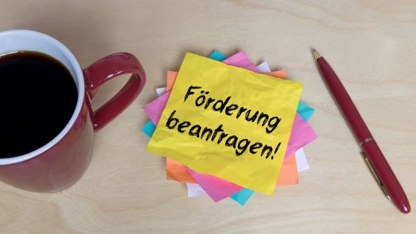 Förderung beantragen! © AdobeStock_434546876 Kaffeetasse, Stift und Post-it mit Text "Förderung beantragen!"